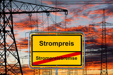 Vor vielen Strommasten mit dramatischen Wolken steht ein Ortsschild mit der Aufschrift Strompreisbremse vs. Strompreis - FOTOMONTAGE
