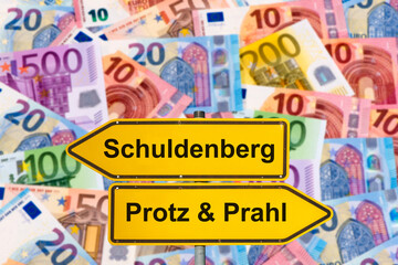 Vor vielen Euro Banknoten steht ein Wegweiser mit der Aufschrift Schuldenberg vs. Protz & Prahl - FOTOMONTAGE