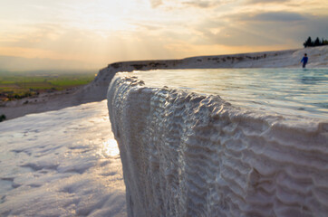 Pamukkale, Turkey: Sunset illuminates white travertine terraces and thermal pool. Unique geological formations created by mineral-rich geothermal waters flowing down natural cascades. 