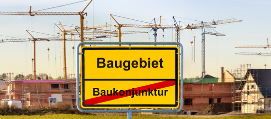 Vor einem Neubaugebiet mit vielen Baustellen und Baukränen steht ein Ortsschild mit der Aufschrift Baukonjunktur und Baugebiet - FOTOMONTAGE