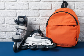 Pair of roller skates and backpack on blue table near white brick wall
