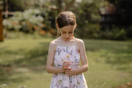 Naklejki Young girl looking down on the flower she's holding