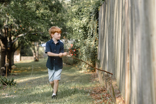 Young boy running a piece of stick along a wooden fence