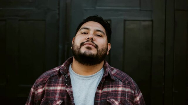 Contemplative urban portrait of bearded man in plaid shirt against dark backdrop