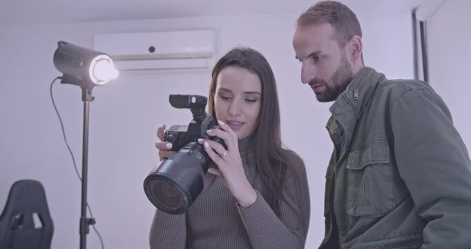 Photographer showing his assistant how to adjust settings on a professional DSLR camera in a photo studio.