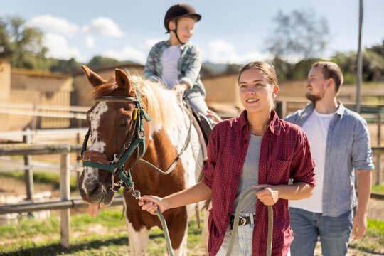 Young woman leads horse on leash with boy rider in paddock