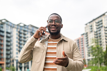 Young man talks on phone while gesturing outdoors in urban setting with modern buildings in the...