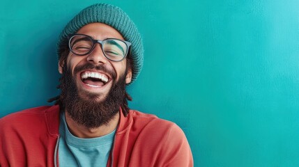 This image captures a joyful man with glasses and a winter hat, radiating happiness against a striking teal background, embodying carefree spirit and positivity.