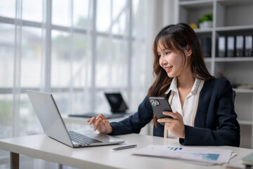 Fototapeta premium Asian businesswoman using laptop and smartphone working in office