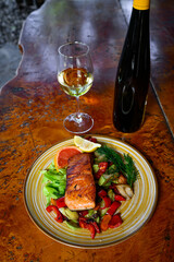 Baked salmon garnished with lemon, pepper and tomatoes with herbs and with a bottle and a glass of wine