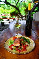 Baked salmon garnished with lemon, pepper and tomatoes with herbs and with a bottle and a glass of wine