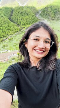 4K Vertical selfie shot of Indian girl enjoying summer holidays in mountains in Sural Bhatori, Himachal Pradesh, India. Travel, tourism and hiking outdoors concept. Girl having fun while trekking. 