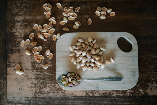 Pistachios on a wooden chopping board with metal spoon top down