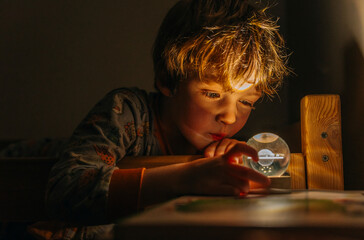 boy lies in his bed in pajamas and looks at the night light with the planet saturn before going to...