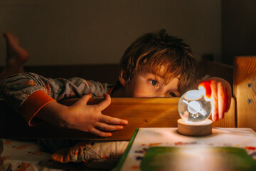 boy lies in his bed in pajamas and looks at the night light with the planet saturn before going to...