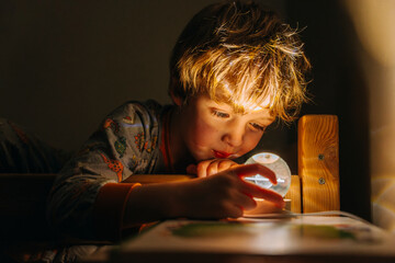 boy lies in his bed in pajamas and looks at the night light with the planet saturn before going to...