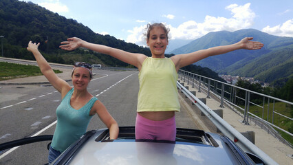 Woman mother and a girl are standing on the roof of a car. The girl is wearing a yellow shirt in...
