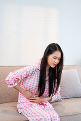 Young woman suffering from strong abdominal pain while sitting on sofa at home.