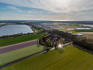 Aerial view of vibrant tulip fields in full bloom stretching along a calm canal, with farmland and...