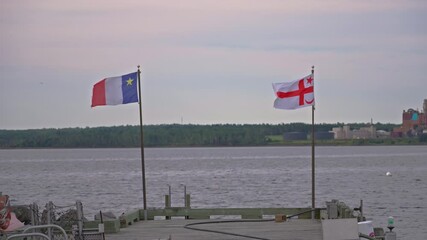 Acadian and Mi'kmaq flags waving along waterfront dock in tranquil scene