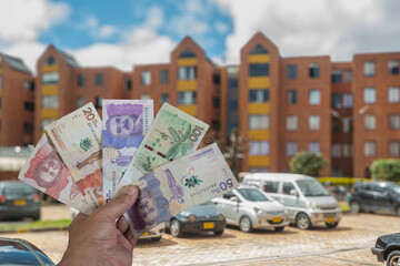 Colombian peso bills in a man's hand in front of a parking lot and apartment buildings