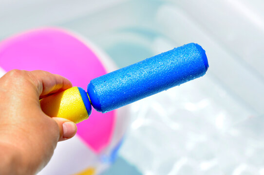 Hand holding a colorful foam water toy over an inflatable pool. - Powered by Adobe
