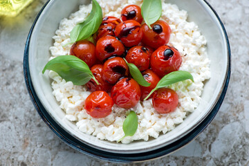 Bowl of caprese with cottage cheese, roasted cherry tomatoes and fresh green basil, horizontal shot, middle closeup