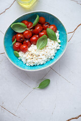 Cottage cheese caprese with roasted tomatoes and green basil, vertical shot on a white stone background with space, top view