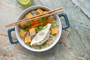 Rice noodles with smoked tofu and steamed dumpling, horizontal shot on a grey and roseate granite background, above view