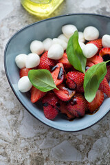Bowl of caprese with fresh strawberry, mini mozzarella, fresh basil and balsamic vinegar, vertical shot, middle close-up