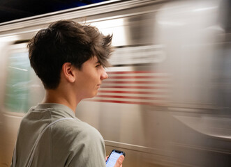 Young man waiting for new york subway train while using smartphone