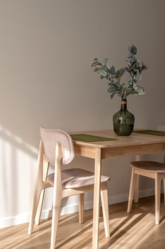 Warm cozy dining room in Mediterranean style, light beige wooden table and chairs, green vase with olive tree branch, natural sunlight shadows on beige wooden wall, modern apartment interior design