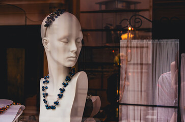 A mannequin head wearing a blue necklace. The necklace is made of beads. The mannequin is in a store window