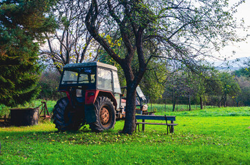 A tractor is parked in a field next to a tree. There is a bench in the field