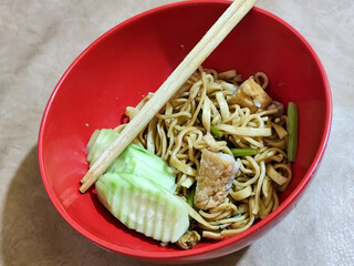 A bowl of chicken noodles with fresh cucumber slices, tofu pieces and celery sticks, served with...
