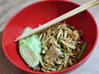 A bowl of chicken noodles with fresh cucumber slices, tofu pieces and celery sticks, served with...