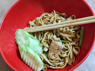 A bowl of chicken noodles with fresh cucumber slices, tofu pieces and celery sticks, served with...