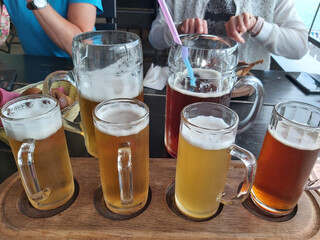 Wooden tray with four glasses of beer on it. One of the glasses is labeled with a logo and two big...