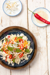 Colourfull Asian salad with cabage on a dark plate with chopsticks and red pepper in the background on a wooden table