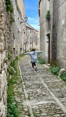 Girl running on old street near building made by stone in anciet town. Happy person travel on Sicily in Erice. Vertical.