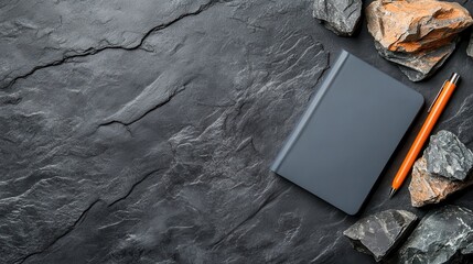 A dark notebook lies on a textured black stone background, surrounded by rough stones, creating a minimalist and sophisticated aesthetic.