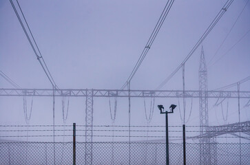 A fence with wires and poles in the background. A man is standing in front of the fence