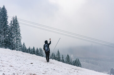 A person is walking on a snowy hill. The person is wearing a black jacket and a backpack