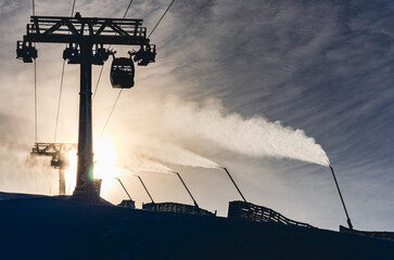 A ski lift is in the background of a snowy mountain. The ski lift is in the foreground of the image