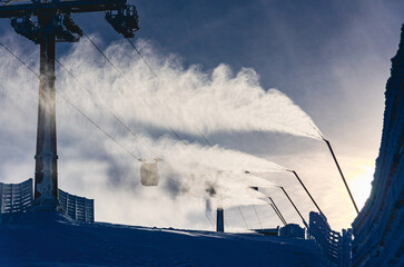 A ski lift is spraying water onto the snow, creating a misty atmosphere. The water is coming out of the ski lift and is falling onto the snow, making it wet and slippery