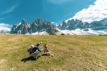 Hiker with dog enjoying scenic view of snowy mountain peaks in the Dolomites, Italy.