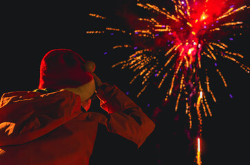 A person in a red hat is watching fireworks in Christmas time. Santa cap