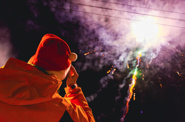 A person in a red hat is watching fireworks. The fireworks are in the sky and are colorful