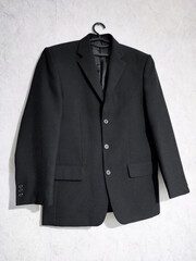 Black man's jacket on hanger isolated on gray textured background. Three buttons turn down collar...