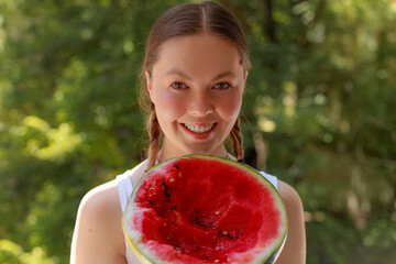 Joyful girl with braids and freckles smiles wide while presenting juicy watermelon slice, greenery...